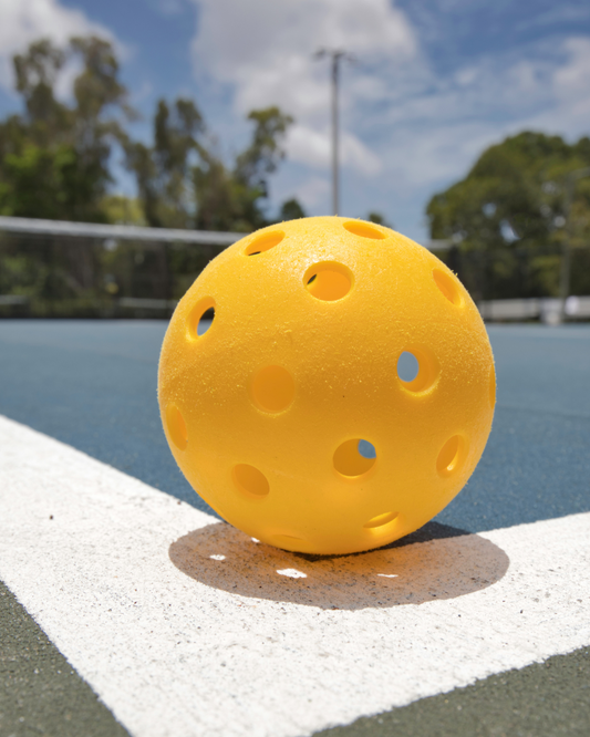 Selection of indoor and outdoor pickleball balls on a court, ready for play